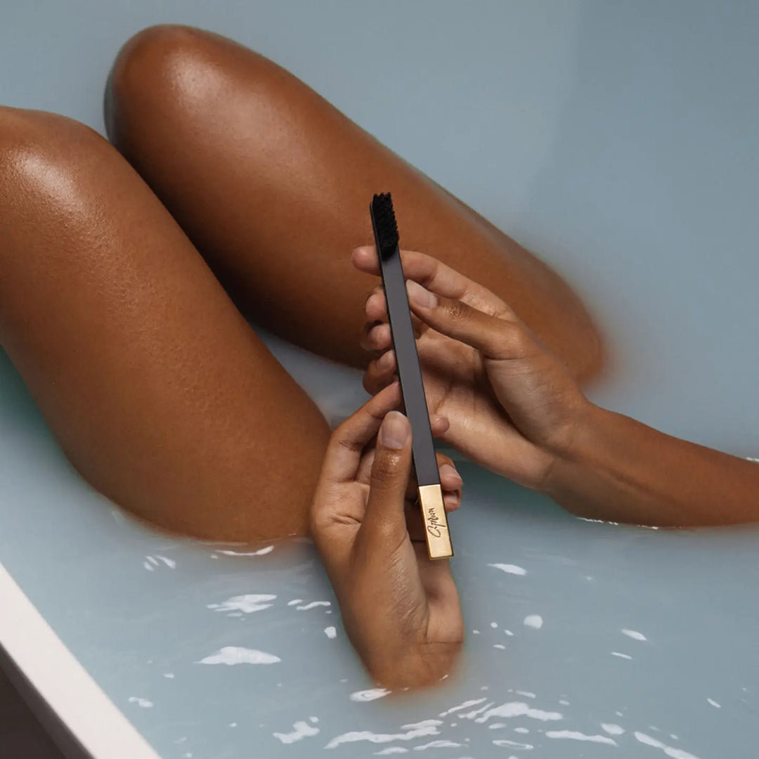 Person holding a black and gold brush with water and legs in the background