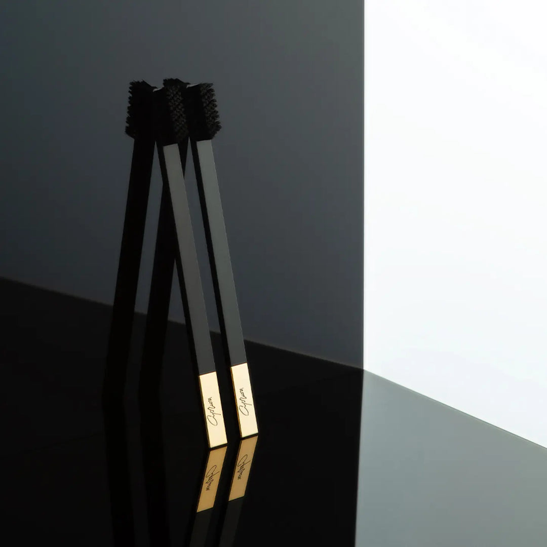 Two black toothbrushes with gold accents on a reflective surface