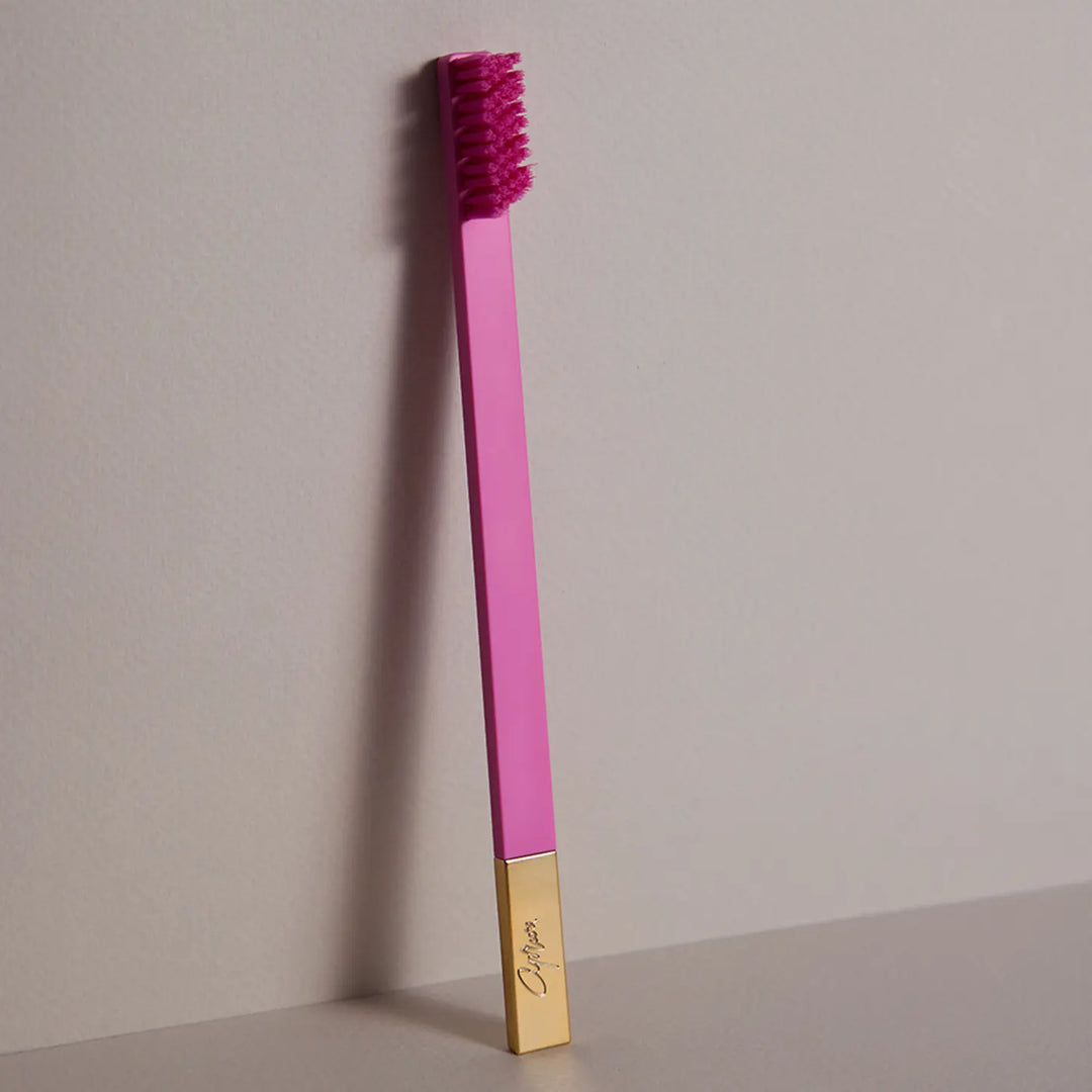 Pink toothbrush with gold base on a gray background