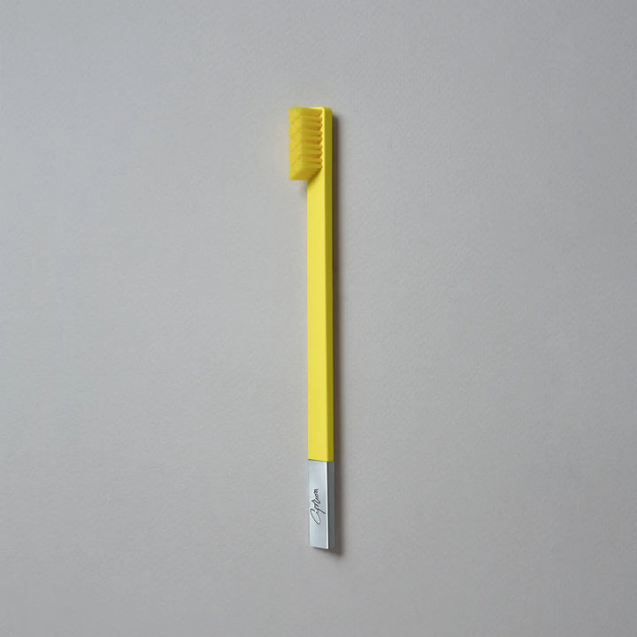 Yellow toothbrush with a silver handle on a gray background