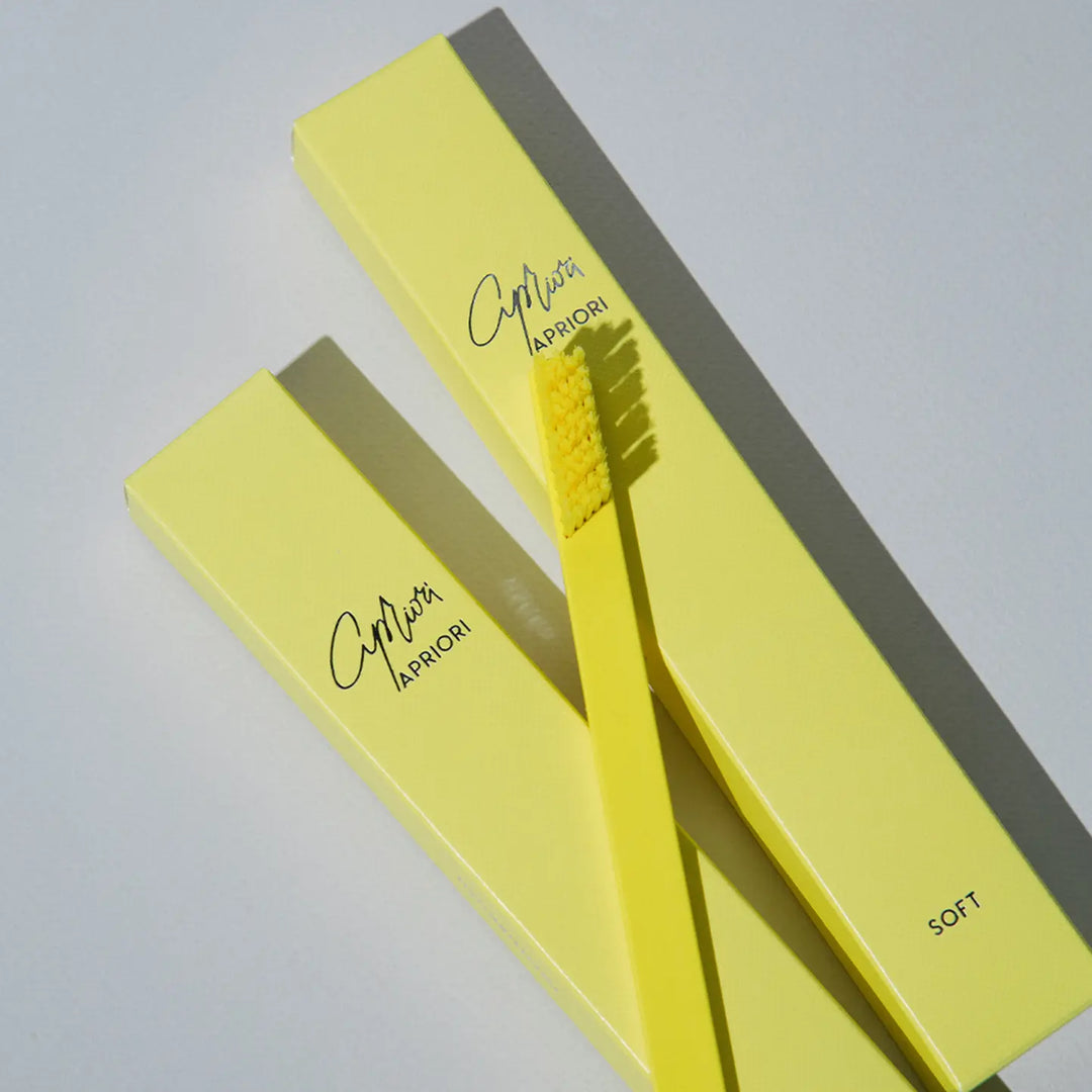 Yellow toothbrush with soft bristles and packaging on a light gray background