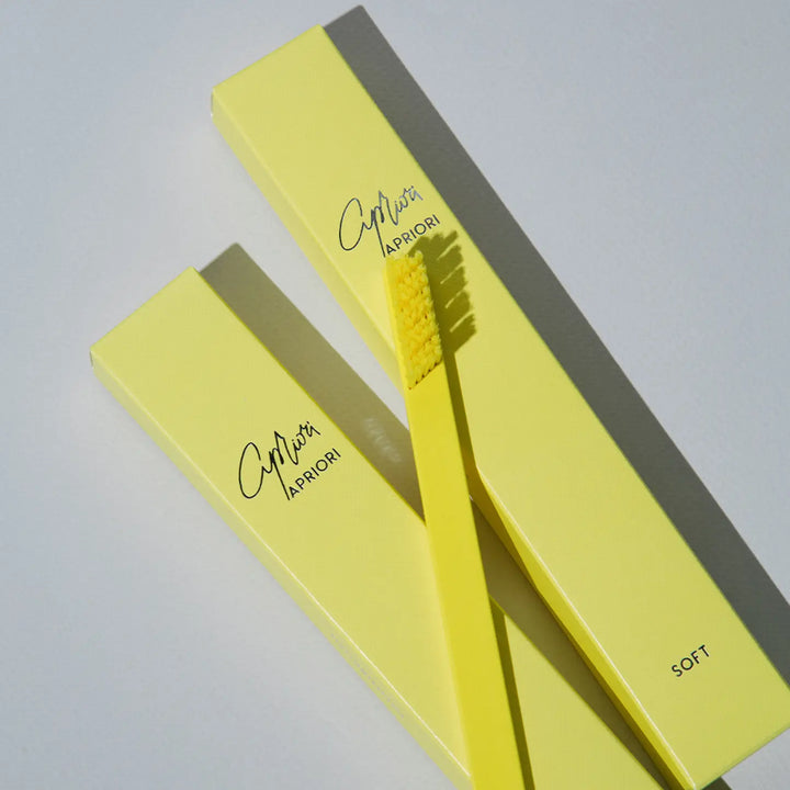 Yellow toothbrush with soft bristles and packaging on a light gray background