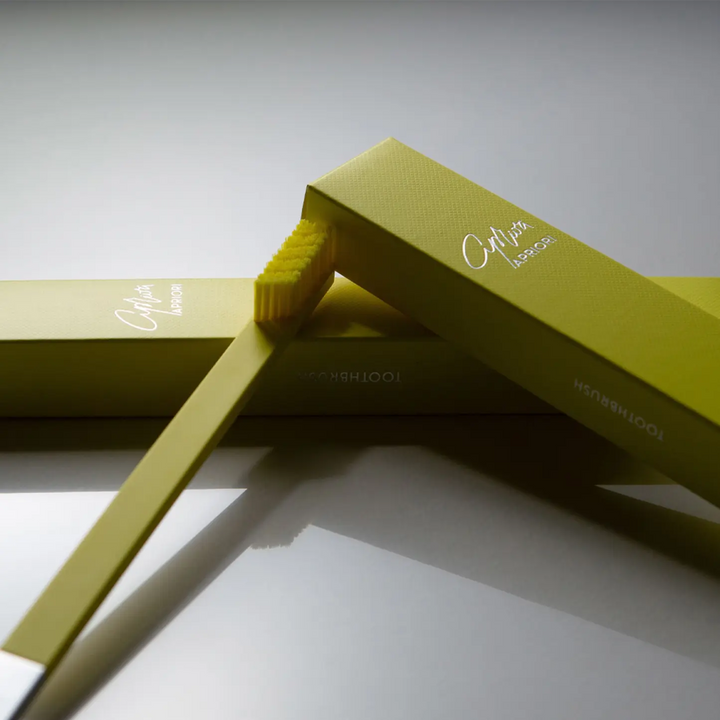 Yellow toothbrush with packaging on a light gray background