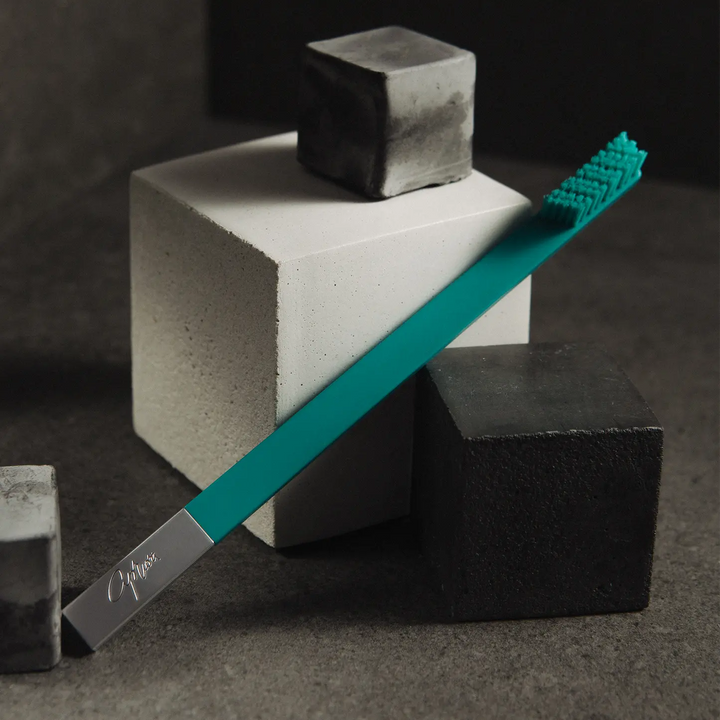 Teal toothbrush with silver handle on geometric stone blocks