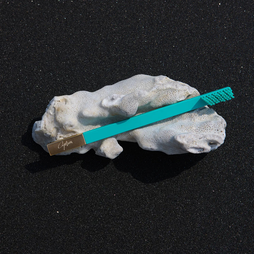 Teal toothbrush on a piece of coral with a dark background