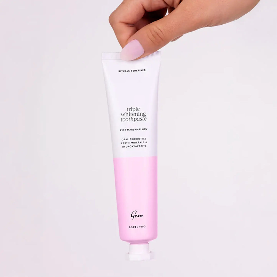 Tube of 'Gem' triple whitening toothpaste held by a hand on a white background