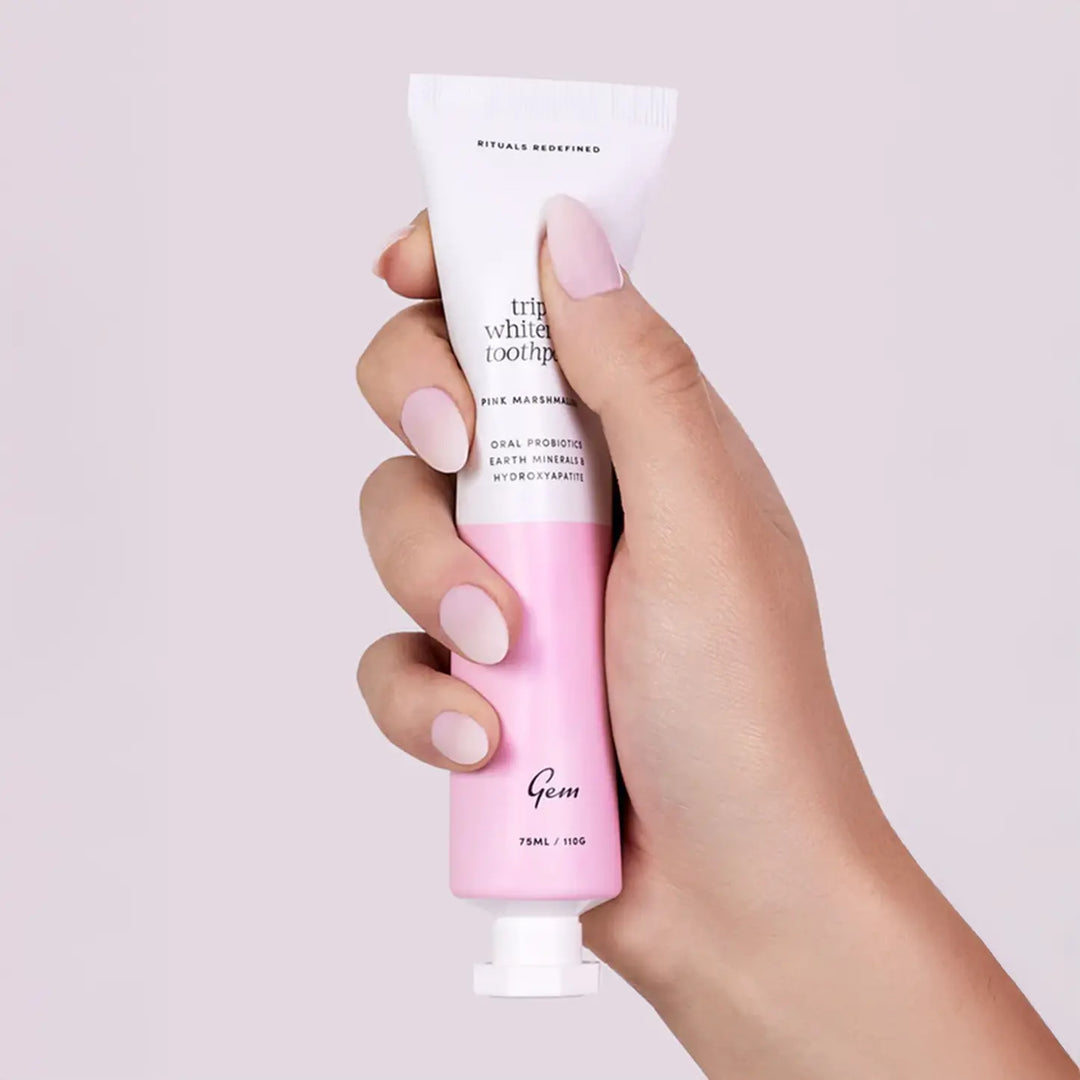 Hand holding a pink and white toothpaste tube with 'Gem' branding on a light background