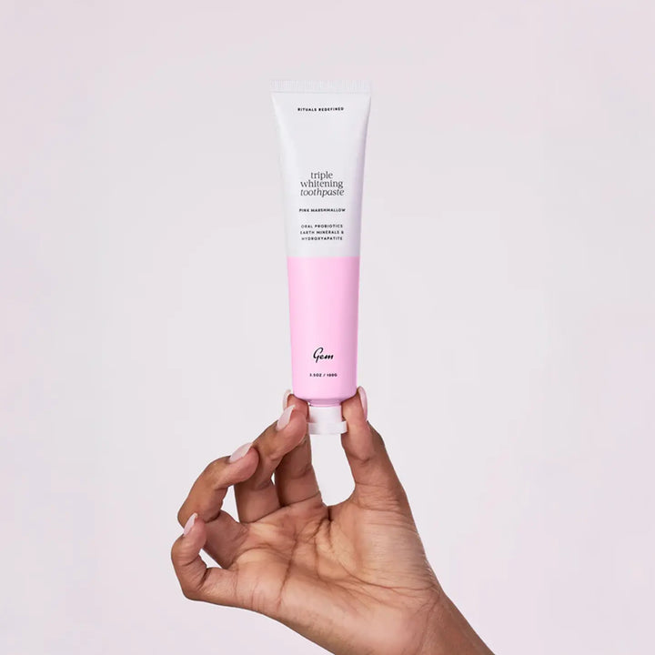 Hand holding a tube of pink and white toothpaste against a light gray background