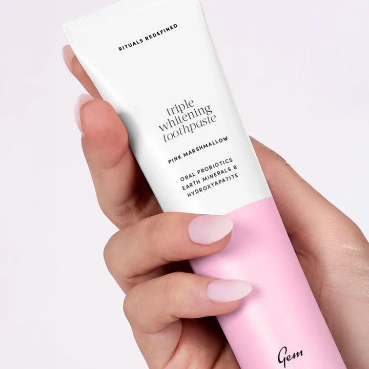 Hand holding a pink and white toothpaste tube with 'Gem' branding on a light background