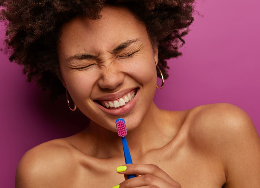 Woman smiling widely clenching toothbrush near chin