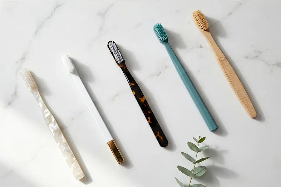 Five premium toothbrushes arranged on white marble — bamboo, ultra-soft, coloured, black, and white designs representing Australia's best manual toothbrushes