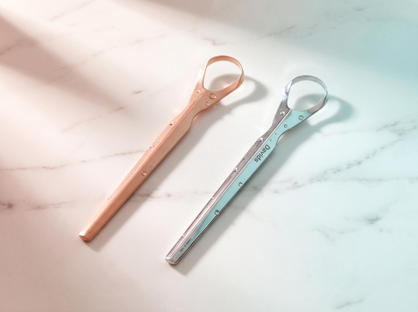 Copper and Davids stainless steel tongue scrapers side by side on marble