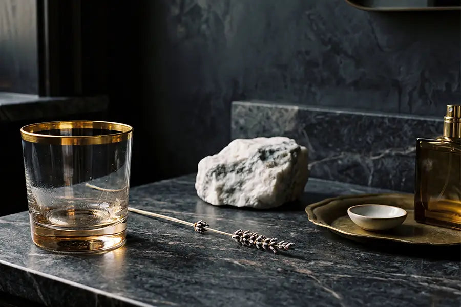 Luxury bathroom still life with gold-rimmed glass and brass tray on dark marble