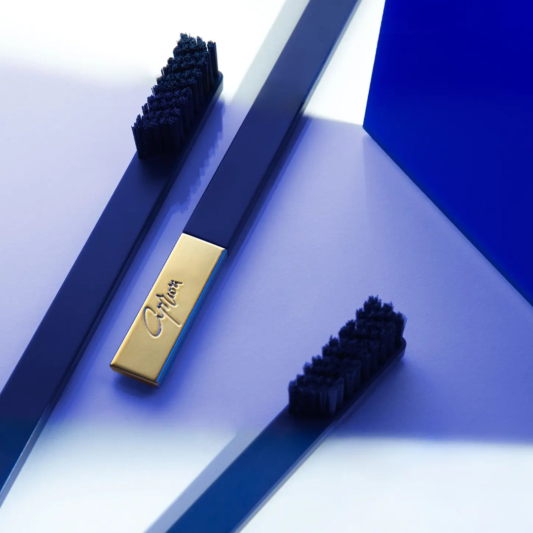Two blue toothbrushes with black bristles and a gold rectangular object on a white and blue geometric background.