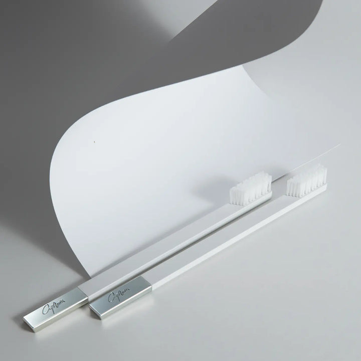 Two white toothbrushes with silver holders on a light gray background