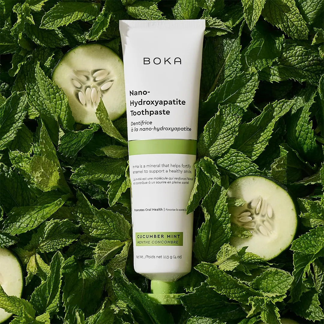 Boka Cucumber Mint toothpaste tube lying on a bed of fresh mint leaves with sliced cucumber rounds