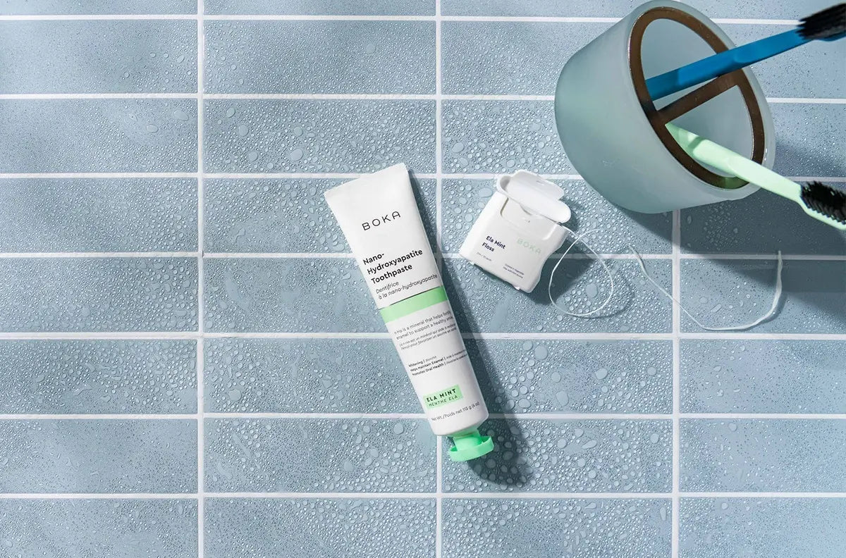 Boka toothpaste tube and dental floss on a tiled bathroom floor