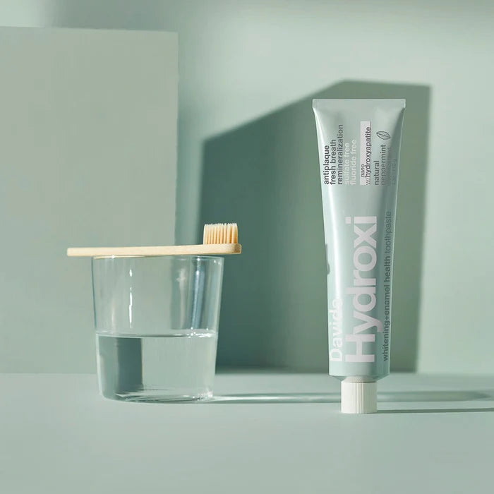 Tube of Perio Hydroxi mouthwash, wooden toothbrush, and glass on a light gray background
