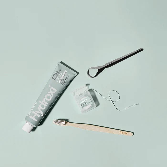 Hydroxi toothpaste tube, wooden toothbrush, and dental floss on a light blue background