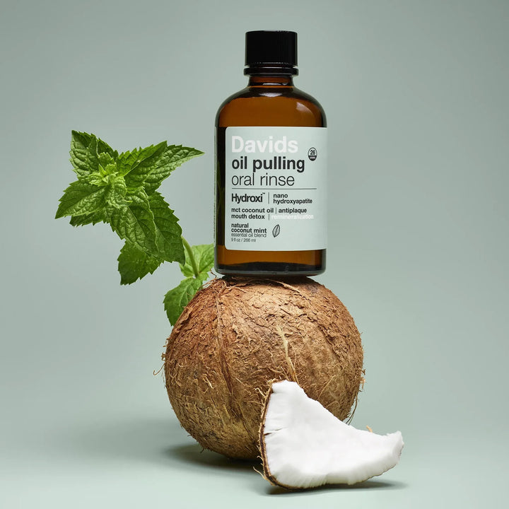 Davids oil pulling coconut oil oral rinse bottle balanced on a coconut with fresh mint leaves