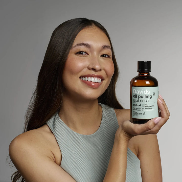 Smiling person holding the Davids oil pulling oral rinse amber bottle