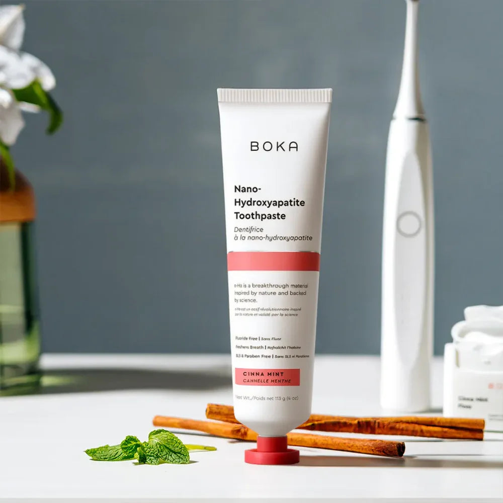 Boka Cinna Mint toothpaste on a bench with cinnamon sticks, fresh mint leaves and an electric toothbrush