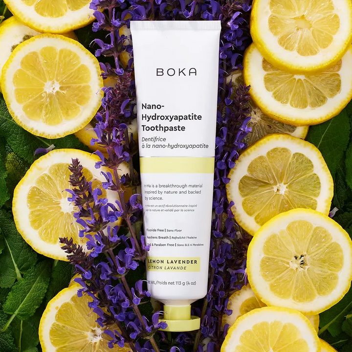 Boka Lemon Lavender toothpaste tube laid on green leaves among lemon slices and purple lavender flowers