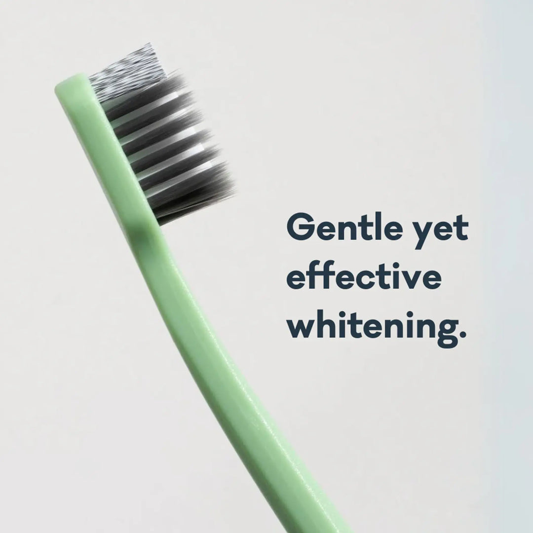 Green toothbrush with black bristles on a light gray background, text 'Gentle yet effective whitening.'