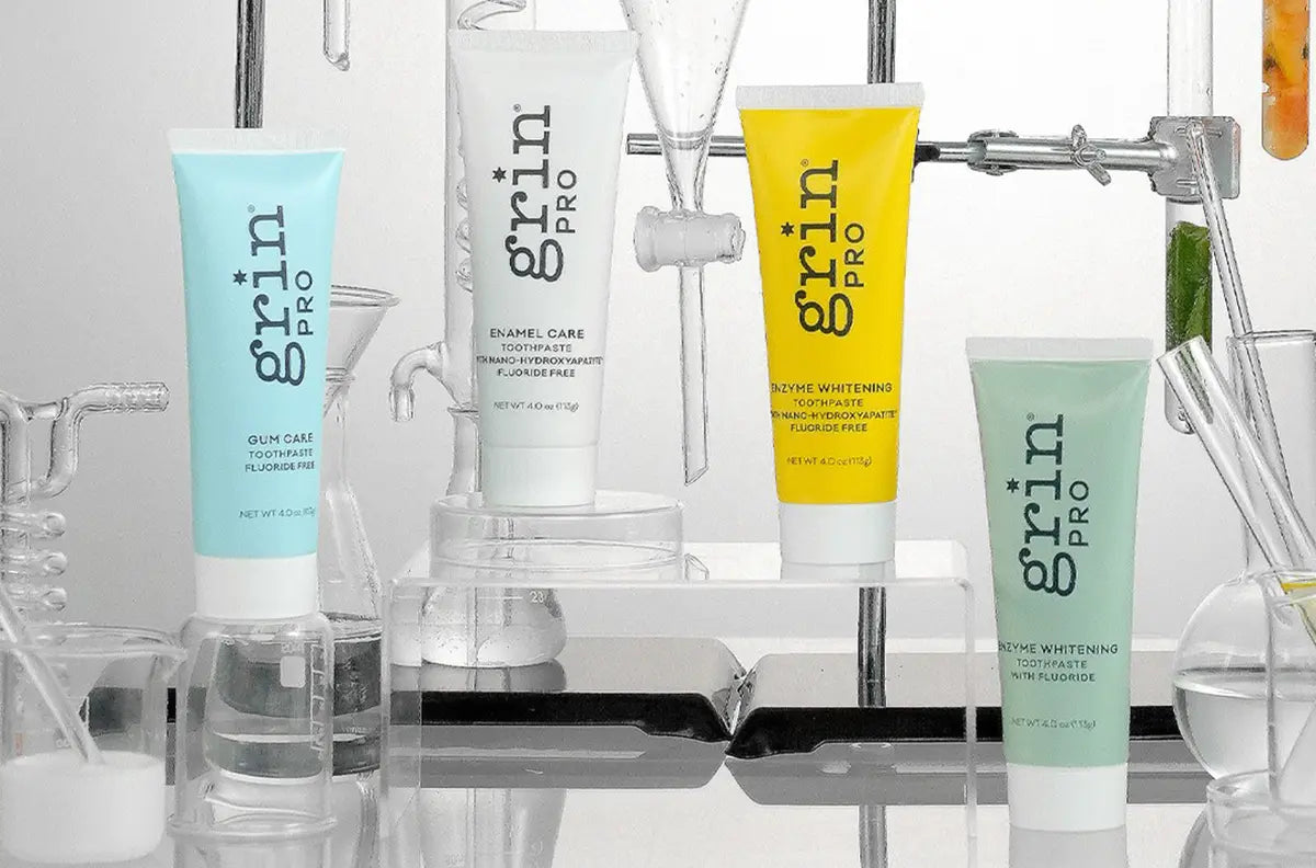 Four 'grin pro' toothpaste products on a laboratory bench with beakers and lab equipment.