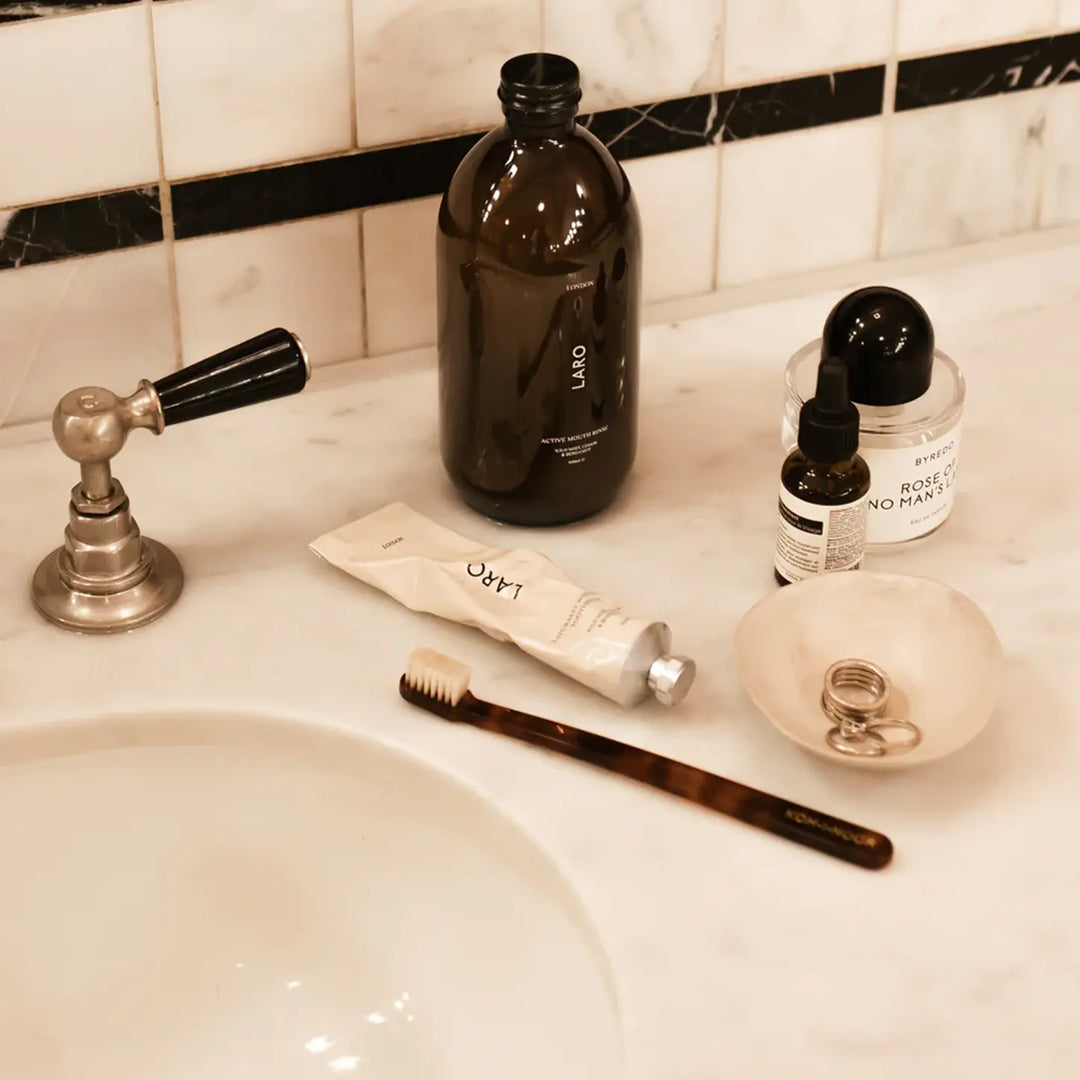Bathroom sink with toiletries including a black bottle, tube of cream, toothbrush, and small bowl.