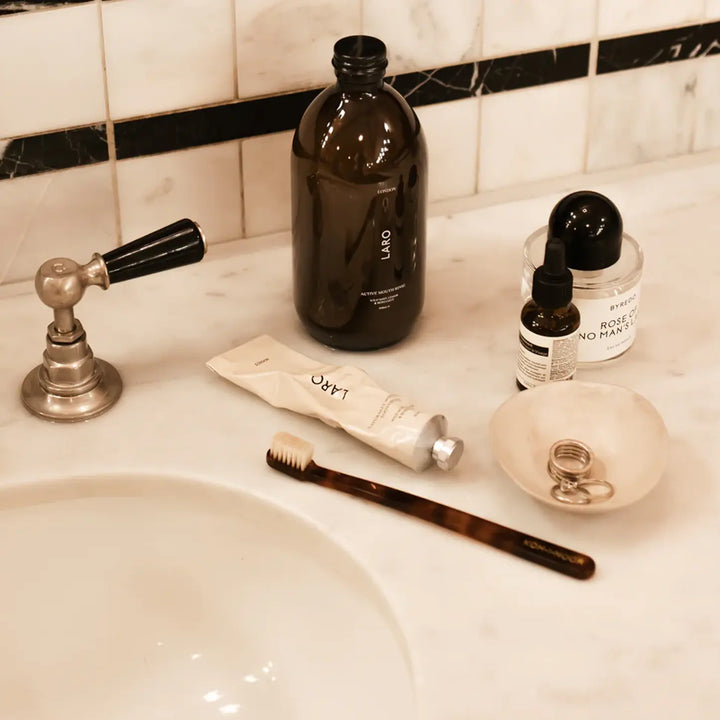 Bathroom sink with toiletries including a black bottle, tube of cream, toothbrush, and small bowl.