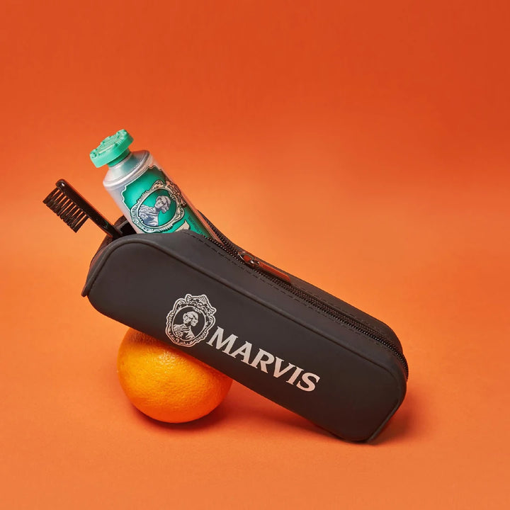 Black Marvis toiletry bag resting on an orange, shown with a Marvis toothpaste and black toothbrush, which are sold separately