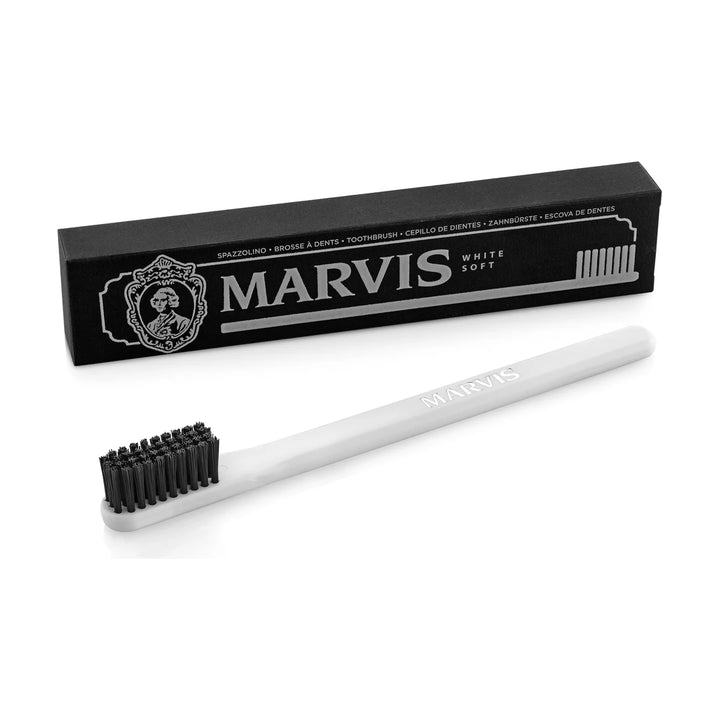 Marvis toothbrush with a white handle, black soft bristles and MARVIS lettering, set before its black box printed White Soft