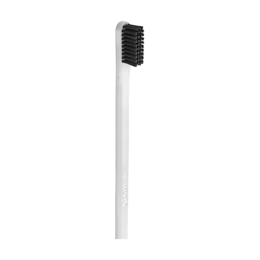 Marvis white toothbrush standing upright on its own: slim white handle, a squared head of black bristles, MARVIS along the stem