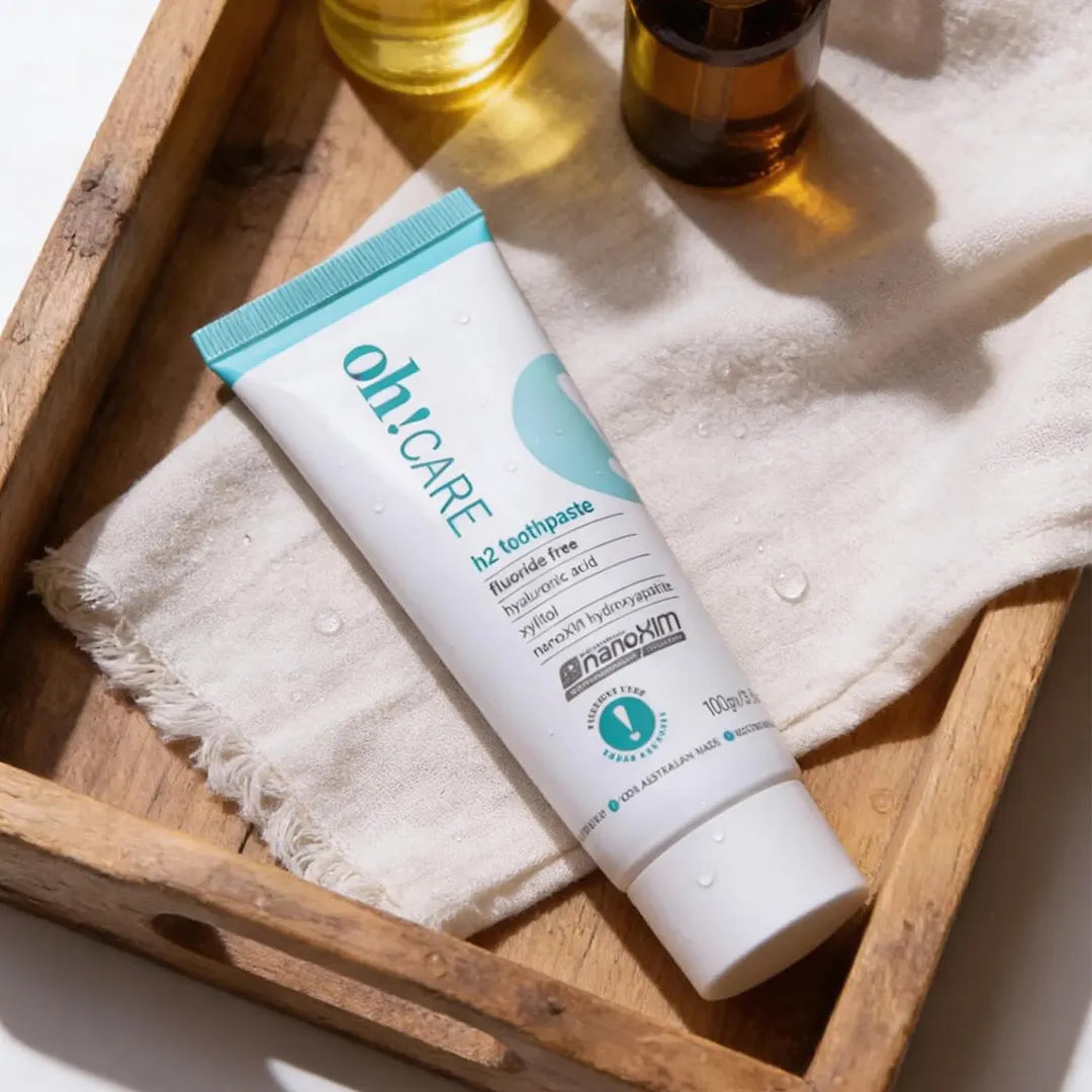 Oh Care h2 fluoride free toothpaste tube held in an open palm against a bright teal background with the Oh Care exclamation mark logo