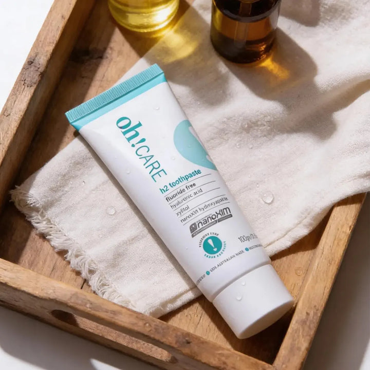 Oh Care h2 fluoride free toothpaste tube held in an open palm against a bright teal background with the Oh Care exclamation mark logo