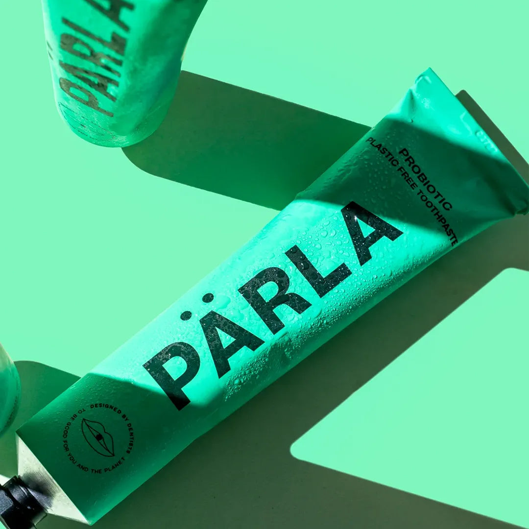 Close up of two PÄRLA Bio Balance probiotic toothpaste tubes with water droplets on the aluminium