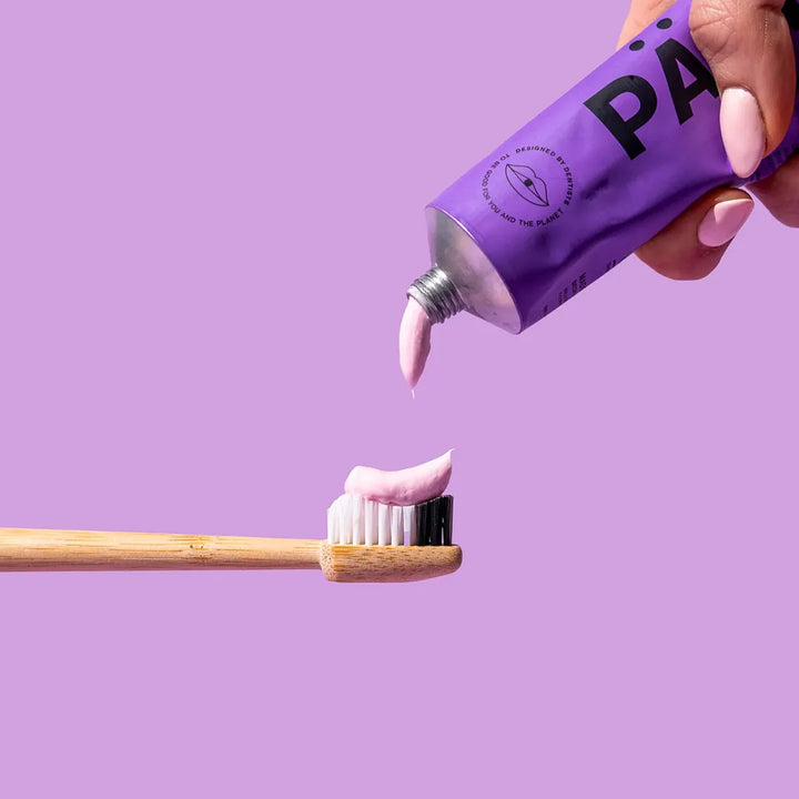 PÄRLA Pro Whitening toothpaste being squeezed from the purple tube onto a bamboo toothbrush
