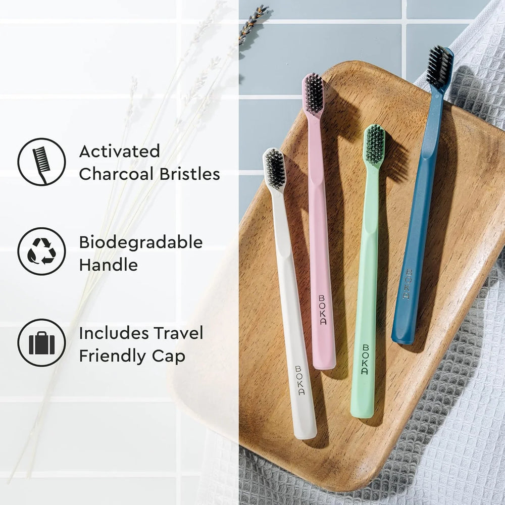 Four toothbrushes in different colors on a wooden tray with text about activated charcoal bristles, biodegradable handles, and travel-friendly caps.