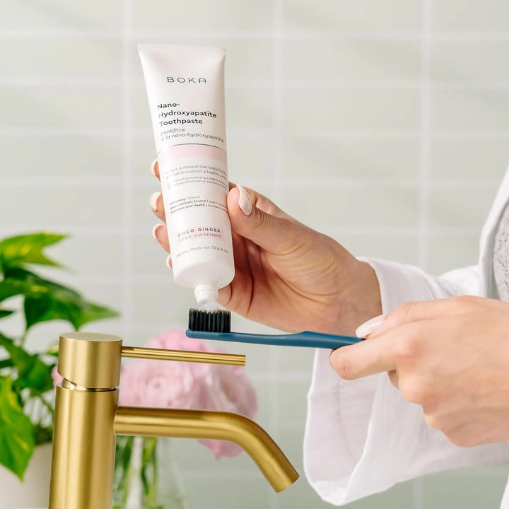 Person applying toothpaste to a toothbrush with a Boka toothpaste tube in the foreground.
