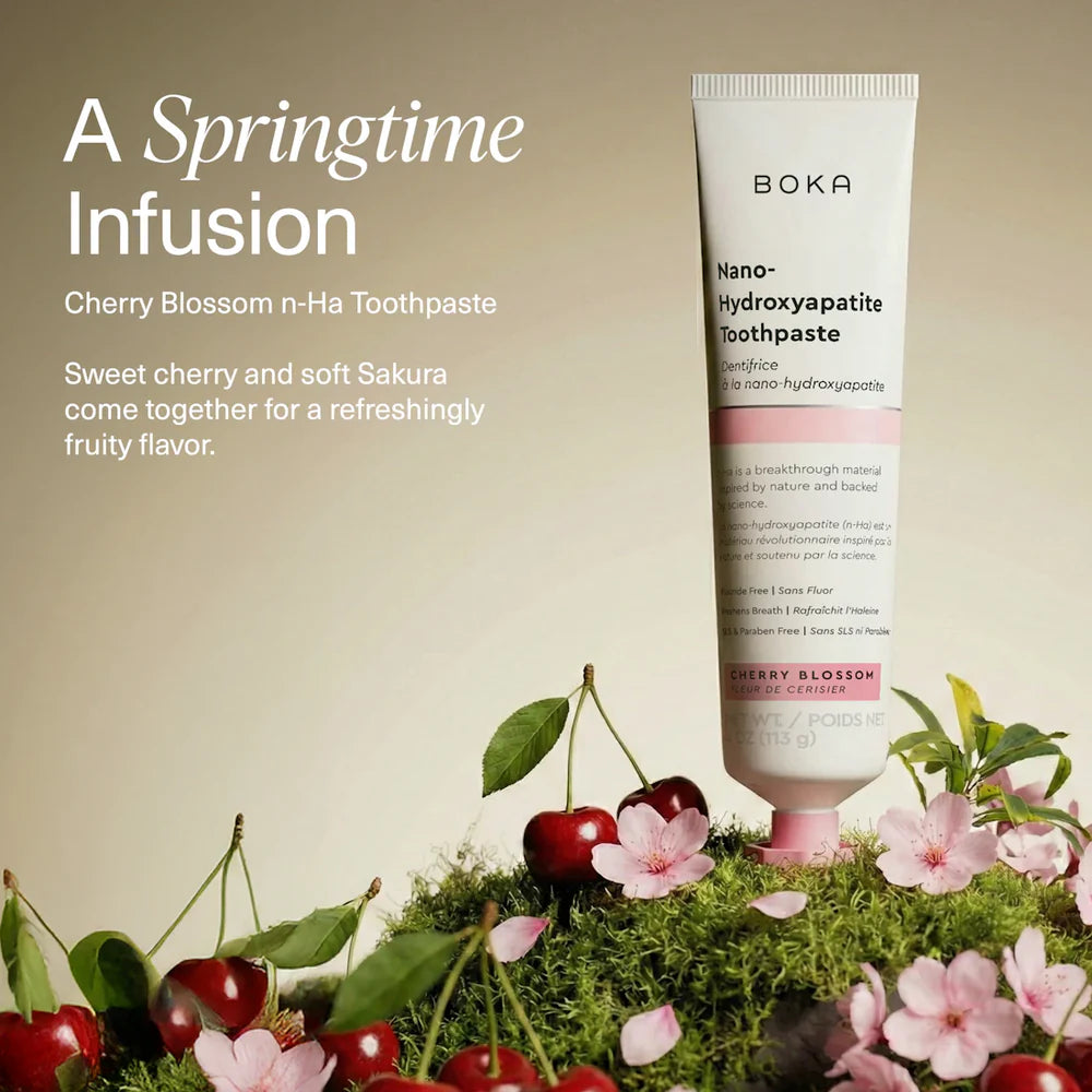 Boka Cherry Blossom toothpaste tube standing on moss with fresh cherries and pink sakura blossoms
