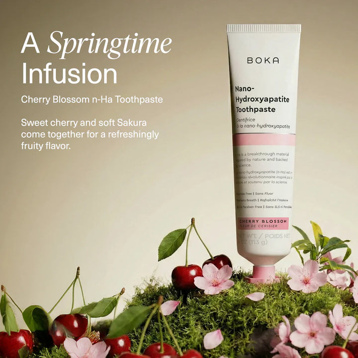 Boka Cherry Blossom toothpaste tube standing on moss with fresh cherries and pink sakura blossoms