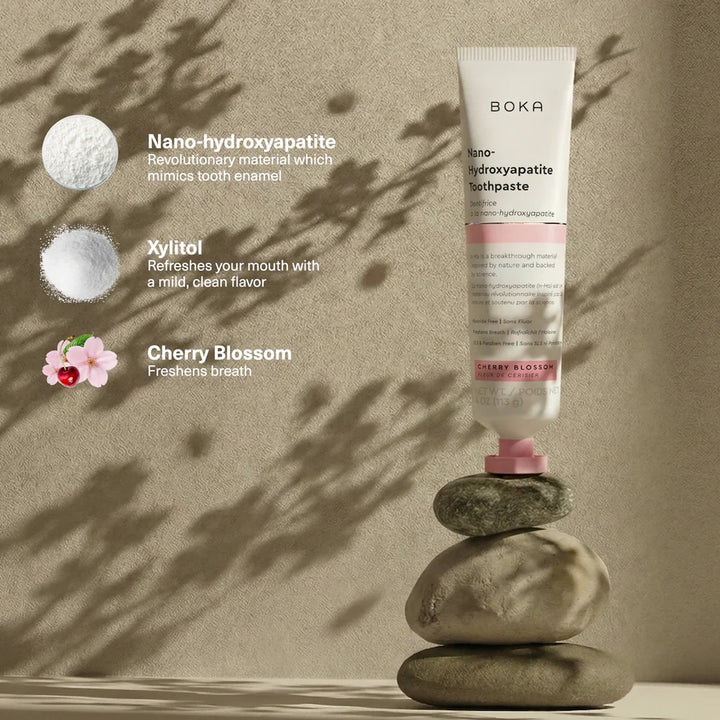 Boka Cherry Blossom toothpaste balanced on stacked stones beside nano-hydroxyapatite and xylitol callouts