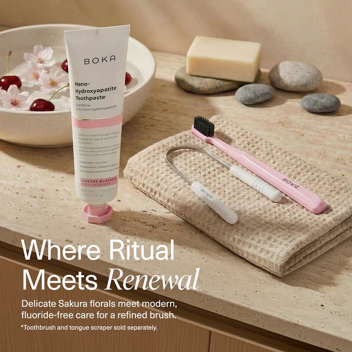 Boka Cherry Blossom toothpaste on a stone bench with a pink Boka toothbrush and tongue scraper