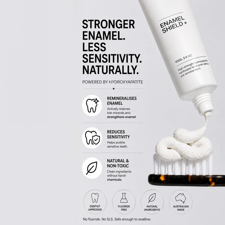 Enamel Shield toothpaste tube with toothpaste being squeezed onto a brush, on a light gray background.