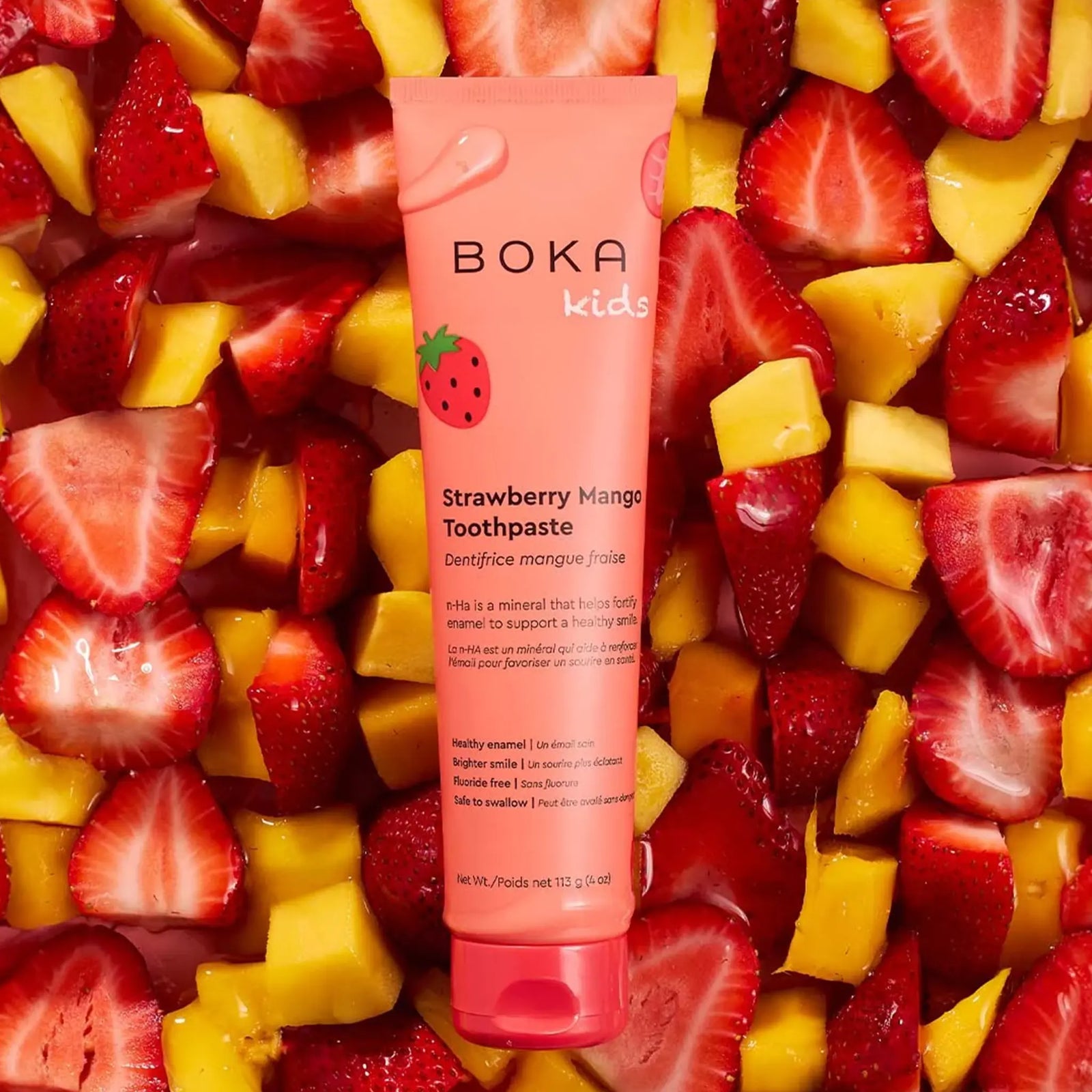 Boka Kids Strawberry Mango toothpaste tube lying on sliced strawberries and fresh mango pieces